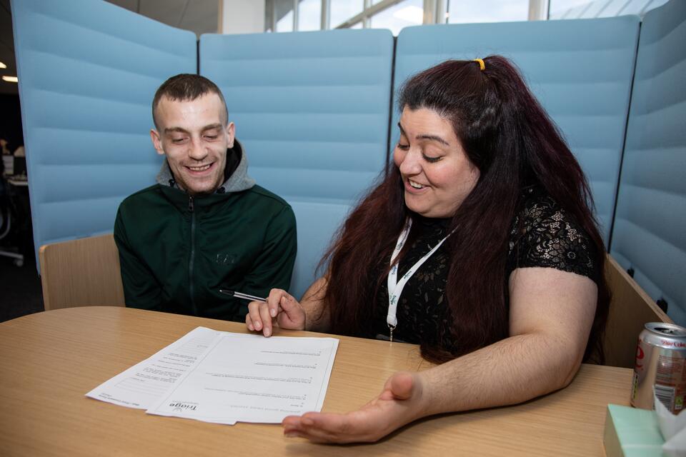 Triage employee helping participant complete an application form. Both smiling.