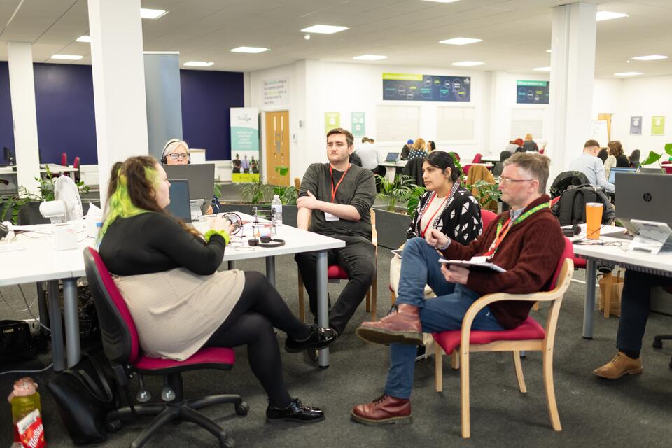 Busy office, one woman chatting to three people at her desk.