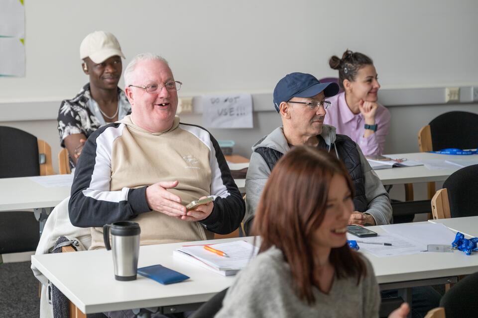 Group of mature students sit in classroom style seating and laughing.