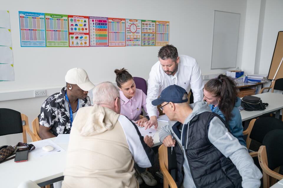 Tutor leaning over a desk of mature students pointing at a document on the table
