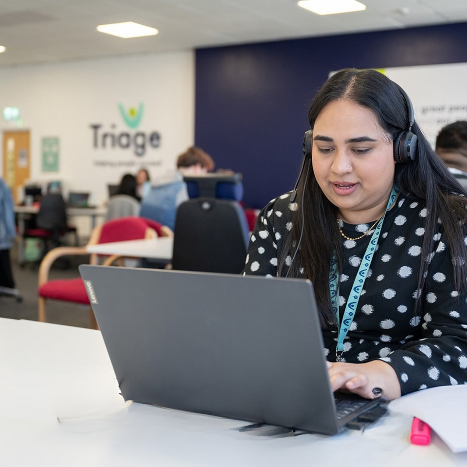 Woman on laptop in busy office wearing headset