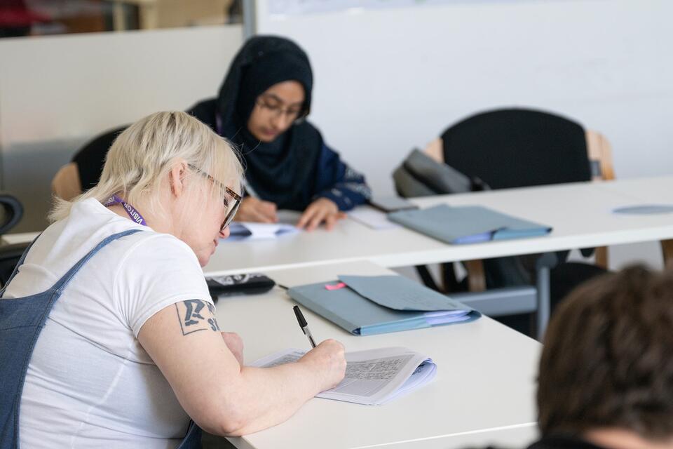 Two women at a table writing in a classroom style setting