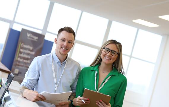 Man and women smiling at camera and holding work files.