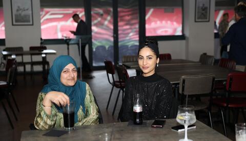 Two women sitting at a table, smiling for the camera. Middlesbrough Football Stadium in background.
