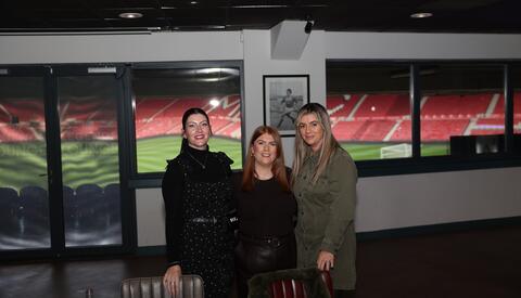 Three women standing for a photo together. In the background is Middlesbrough Football stadium.