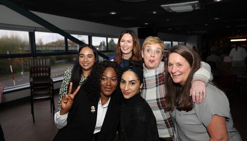 Group of women and huddled together for a group photo laughing and smiling