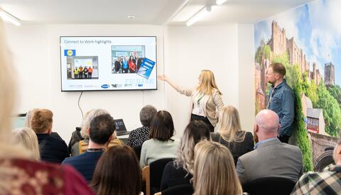 female presenter using powerpoint to present to room of people