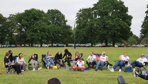 Group of colleagues on the grass in a park, chatting, eating and laughing.