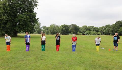 Sack race in a park on grass with trees in the background and grey skies.