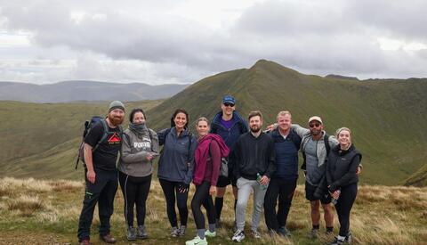Team of male and females at the top of a mountain. Mountain scenes in the background. 