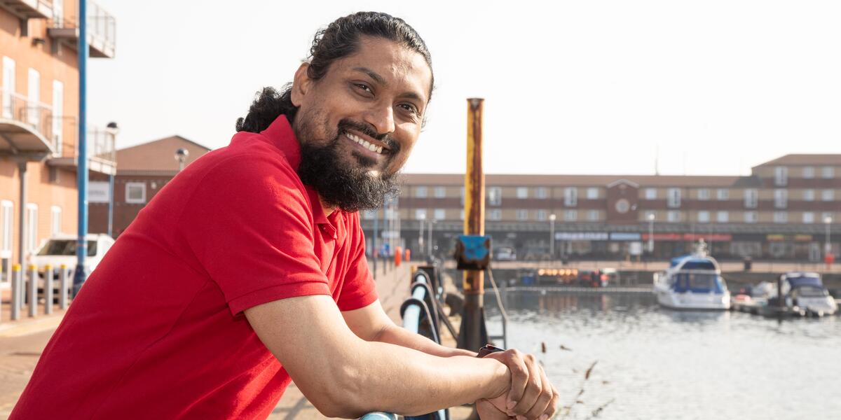 Man in red t-shirt posing by water with boats.