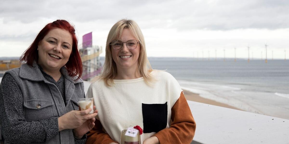 Two women standing by the beach smiling at the camera holding candles. 