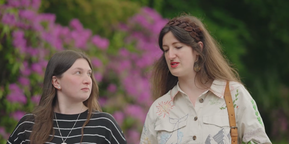 Two women chatting with a bright garden in the background.