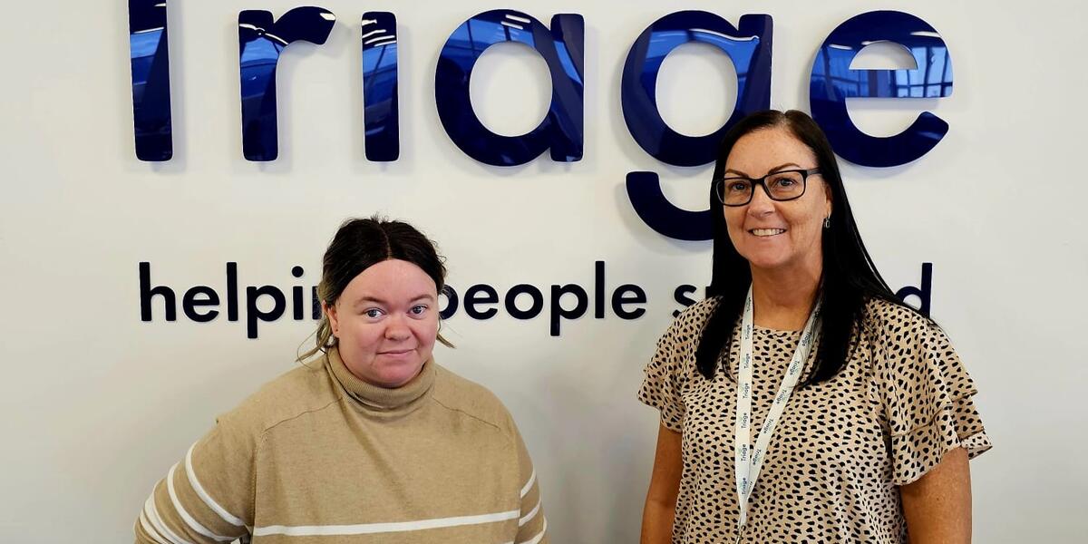 Two women with dark hair smiling with a sign of the Triage logo behind them.