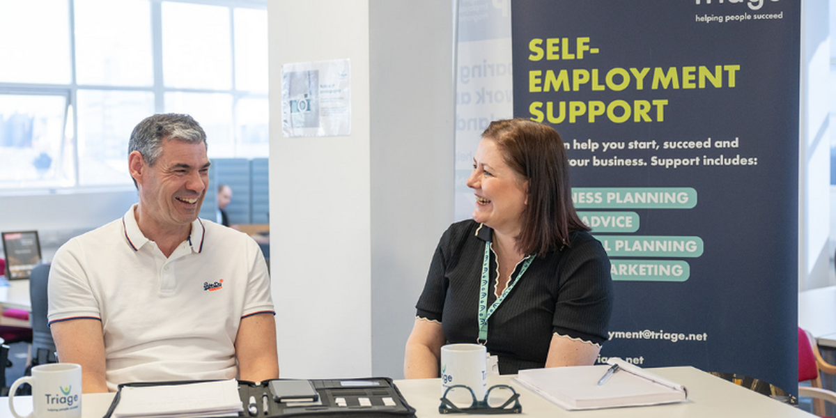Man and woman sitting at a desk in an office, laughing while not looking at the camera