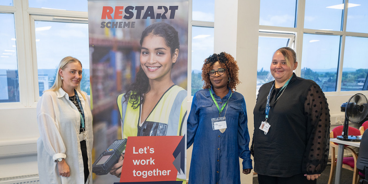 Three women standing beside a Restart pull-up banner smiling for the camera.