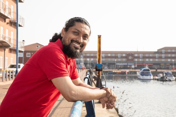 Man in red t-shirt posing by water with boats.