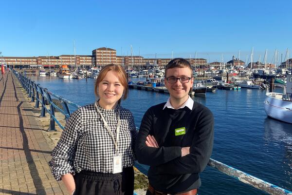 Triage adviser and her male participant standing in front of a sunny marina