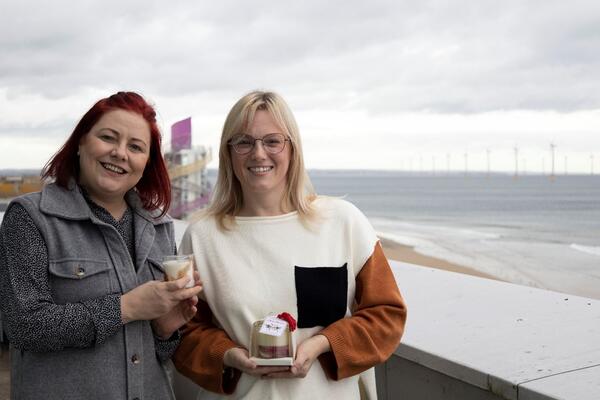 Two women standing by the beach smiling at the camera holding candles. 