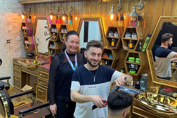 Man standing in a barbers cutting hair. Woman standing beside the barber.