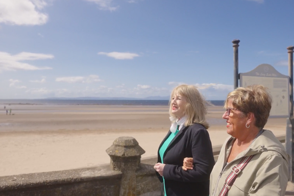 Two women walking and smiling with beach in the background.