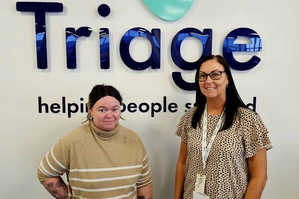 Two women with dark hair smiling with a sign of the Triage logo behind them.