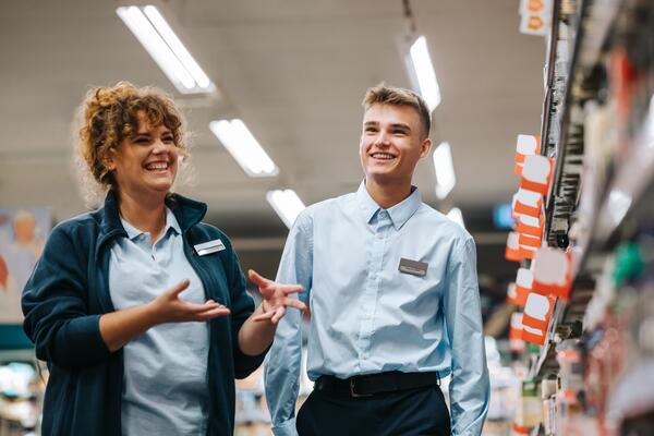 Happy woman mentoring smiley young person on his first day in grocery store