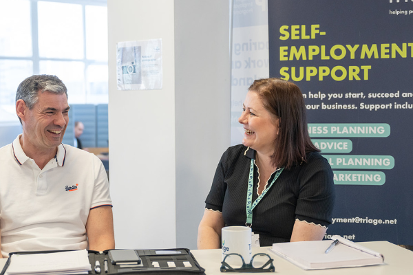 Man and woman sitting at a desk in an office, laughing while not looking at the camera