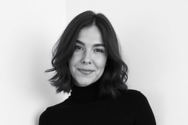 Headshot of a woman with wavy dark hair wearing a black polo neck, smiling at the camera. Image is in black and white.