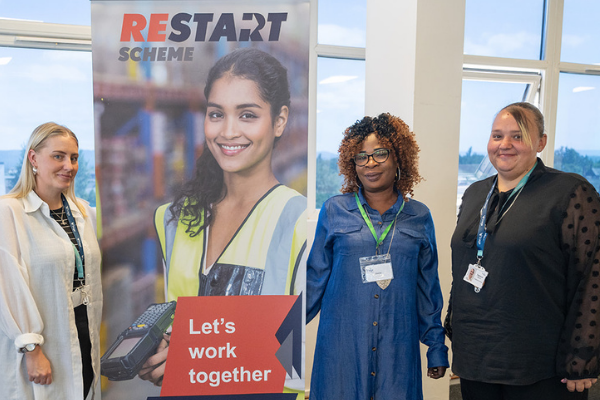 Three women standing beside a Restart pull-up banner smiling for the camera.